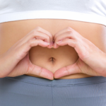 a person holds their hands in the shape of a heart over their navel