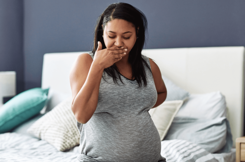pregnant woman sits on a bed with her hand over her mouth